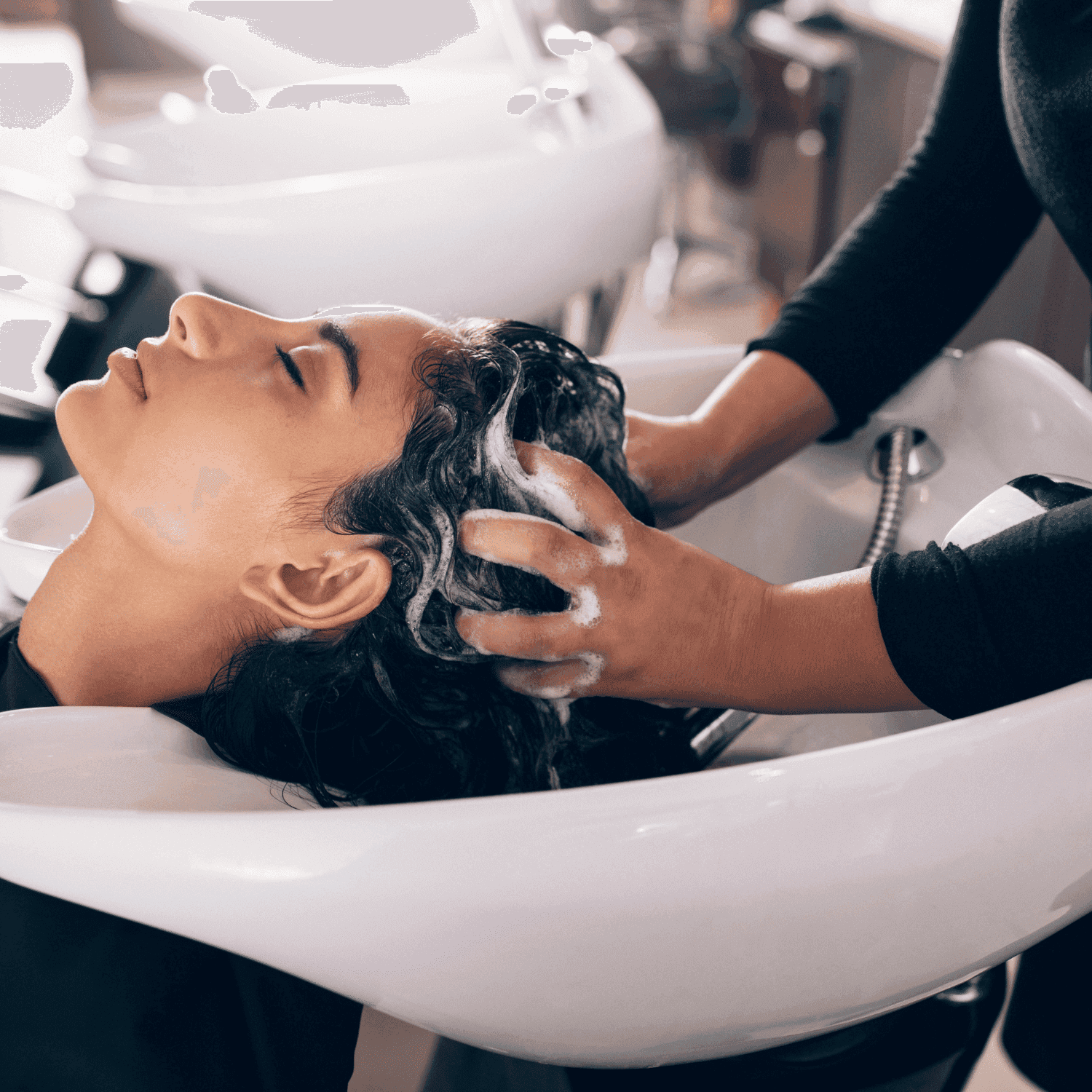 Person getting hair washed at a salon sink by a stylist with foamy shampoo.